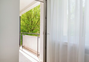 Ein Balkon mit Metallgeländer, einer weißen Wand und einem Baum im Hintergrund.