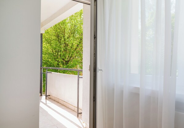 Ein Balkon mit Metallgeländer, einer weißen Wand und einem Baum im Hintergrund.