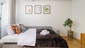 Ett modernt sovrum med en säng, kuddar, ett täcke, en växt och tre inramade tavlor på väggen.