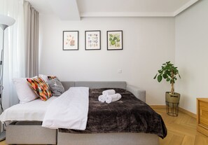 Ein modernes Schlafzimmer mit einem Bett, Kissen, einer Decke, einer Pflanze und drei gerahmten Bildern an der Wand.