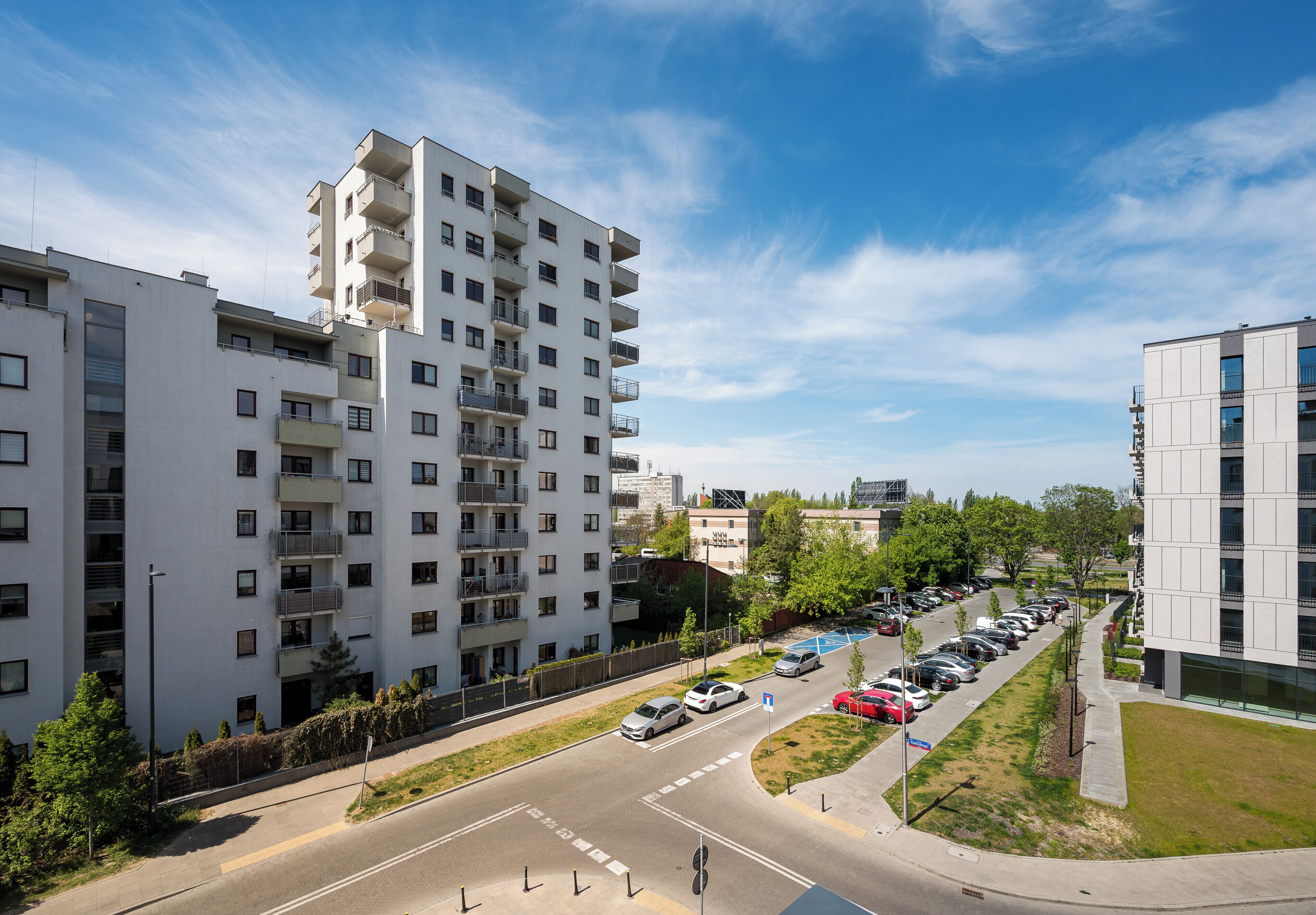 Un edificio residencial de varios pisos con balcones, un estacionamiento con coches y un cielo despejado.