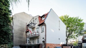 Un immeuble à plusieurs étages doté d’un balcon, d’un drapeau et d’une voiture garée.
