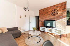 Ein modernes Wohnzimmer mit einer Couch, einem runden Couchtisch, einem Fernseher und einer Wand mit Ziegeln.
