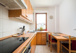 A compact kitchen with wooden cabinets, a stove, a sink, and a dining area with a table and chairs. - Imielin Homely Apartment (Warszawa)