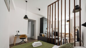 A modern bedroom with a green bedspread, a desk with a chair, a sofa, and a dining area in the background. - Solec Powiśle Chic Apartment (Warszawa)
