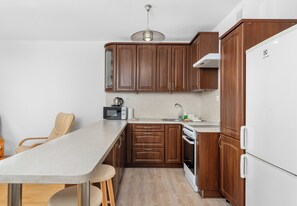 A kitchen with wooden cabinets, a white refrigerator, a microwave, and a dining table with chairs. - Bagry Relax Zone Apartment (Kraków)