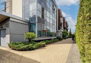 Un edifici modern amb façana de vidre, una passera pavimentada i uns testos de setena correctament tallats.