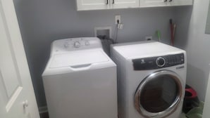 Een wasserette met twee wasmachines, een witte deur en een wit kastje boven de machines.
