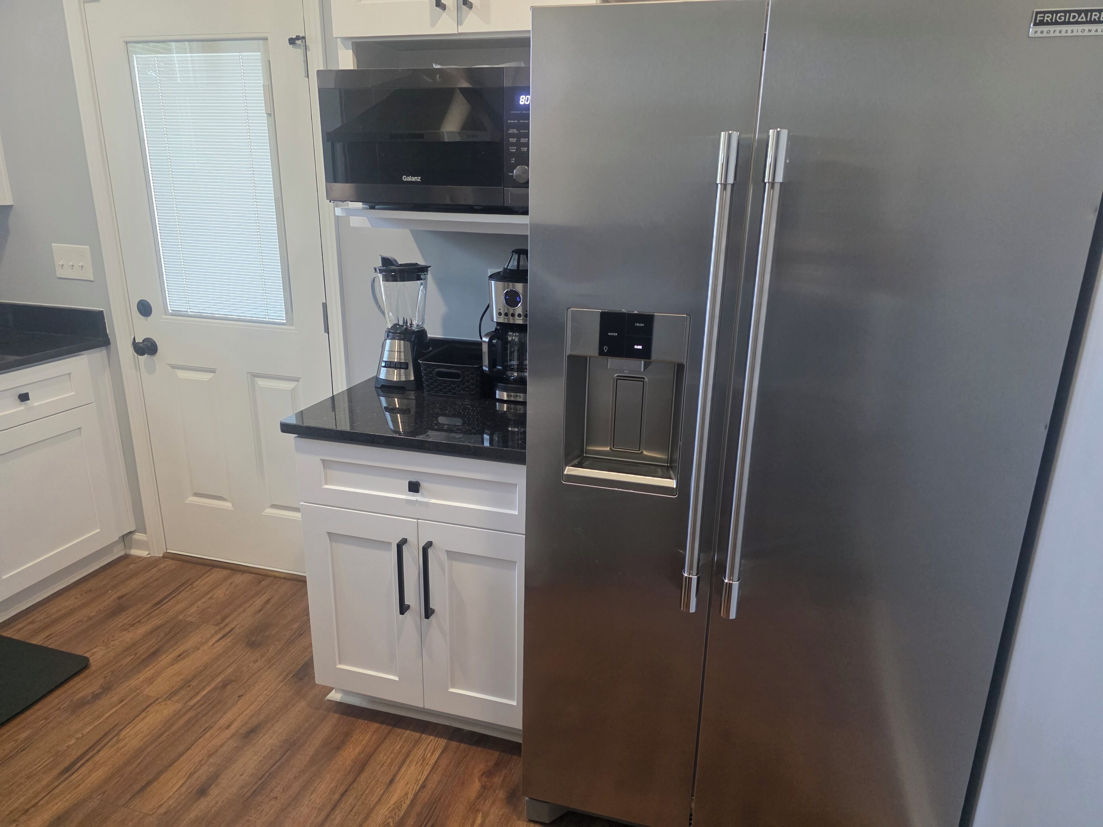 A kitchen with a stainless steel refrigerator, a black microwave, and a water dispenser.