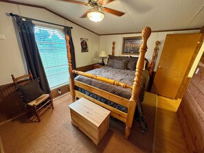 A wooden four-poster bed with a headboard, a wooden bench, a wooden chest of drawers, a ceiling fan, and a door.