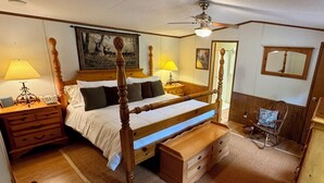 Ein Himmelbett mit Holz Kopfteil, ein Nachttisch mit Lampe, eine Bank am Fußende des Bettes, ein Schaukelstuhl und ein Spiegel an der Wand.