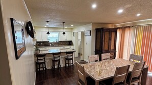 Une cuisine spacieuse dotée d’un îlot central, d’un parquet en bois foncé et d’un coin repas avec une table en marbre et des chaises en bois.