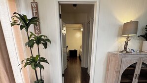 Un couloir avec un plancher en bois, un panneau d’accueil, des plantes en pot et une lampe posée sur un meuble.