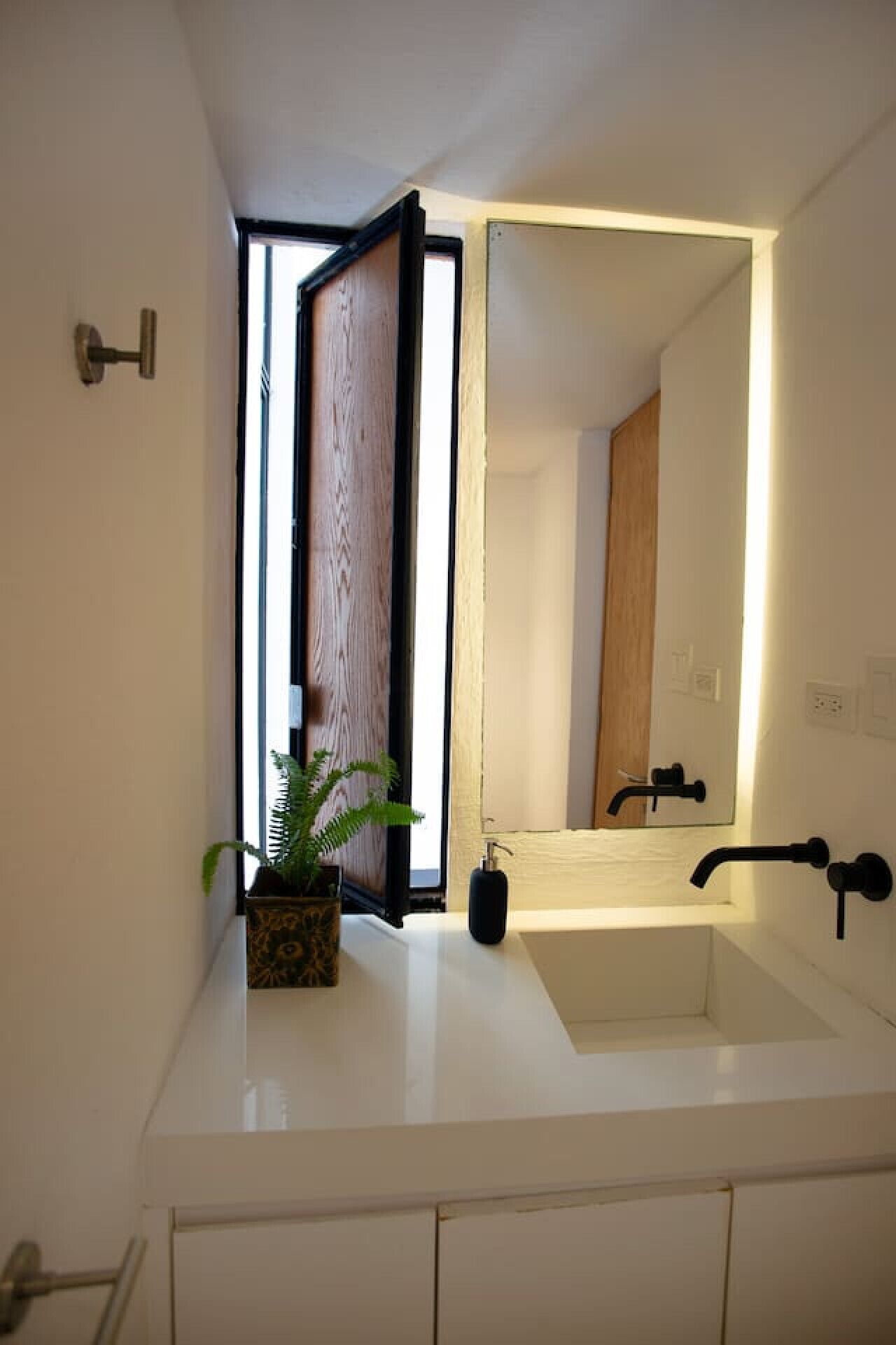 Un baño moderno con un espejo grande, un lavamanos y una planta en maceta.
