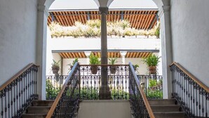 A grand staircase with ornate black railings and wooden handrails, leading to an upper level with a view of a garden.