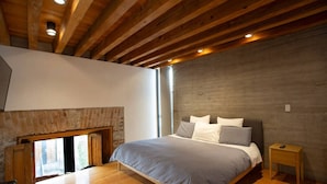 A bedroom with a large bed, wooden beams, a stone fireplace, and a nightstand.