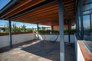 Eine überdachte Terrasse mit zwei Stühlen, Holzboden und Blumentöpfen.