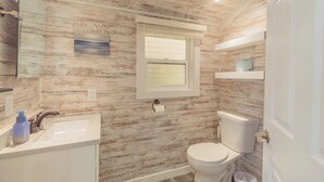 Et badeværelse med trævægsdesign, et håndvask, et toilet og et vindue med persienner.