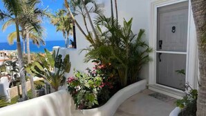 A white building with a curved planter filled with plants and flowers, a door, and a view of the ocean. - Cozy Condo/Ocean view/ Private balcony/Paseo la Jolla/ San Jose del Cabo (San José del Cabo)