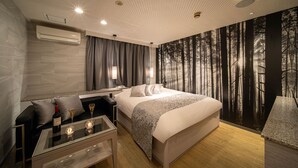 A modern hotel room with a large bed, a seating area with a glass table, and a forest-themed wall mural. - HOTEL KEI - Adults Only  (Himeji)