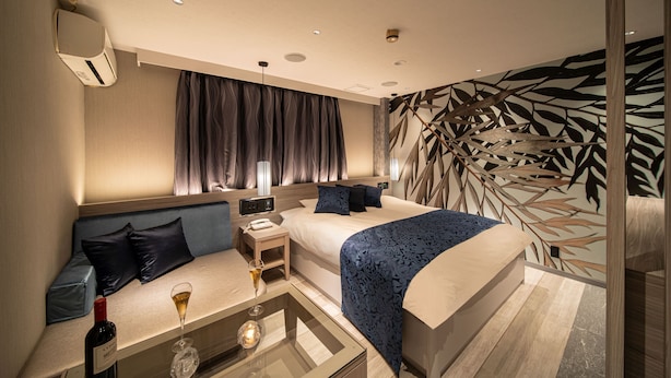 A modern hotel room with a large bed, a seating area with a table, and a decorative wall. - HOTEL KEI - Adults Only  (Himeji)