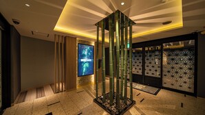 A modern lobby with a central bamboo sculpture, a digital display, and patterned wall decor. - HOTEL KEI - Adults Only  (Himeji)