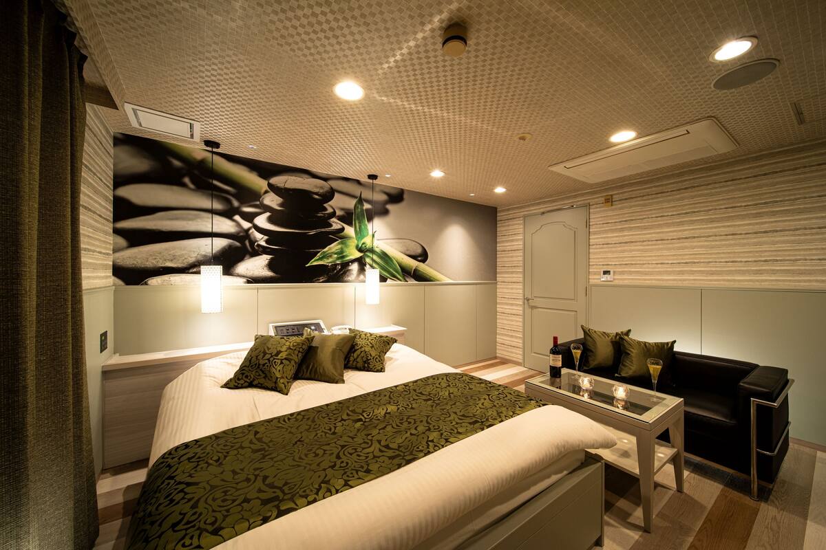 Una habitación de hotel moderna con cama, mesita de noche y zona de estar con sofá y mesa.