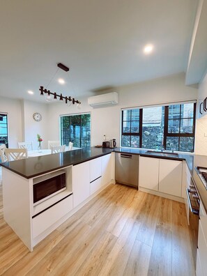 A modern kitchen with a central island, white cabinetry, a built-in microwave, and a large window offering a view of the outdoors. - Bright Home Travel Service at Mt Eden (Auckland)