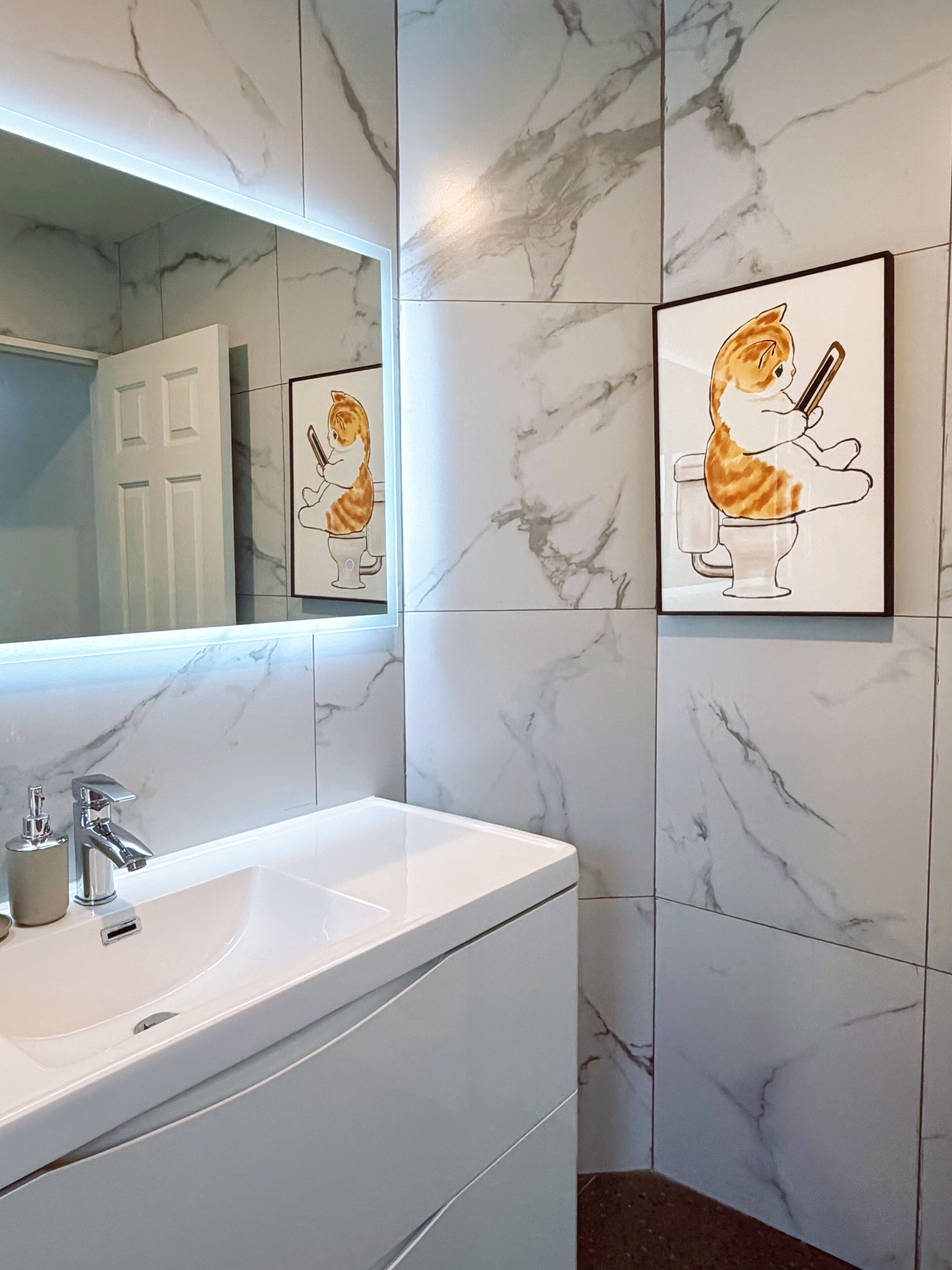 Un baño con pared de mármol, lavabo blanco y fotografías enmarcadas de gatos.