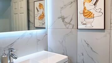 Un baño con pared de mármol, lavabo blanco y fotografías enmarcadas de gatos.