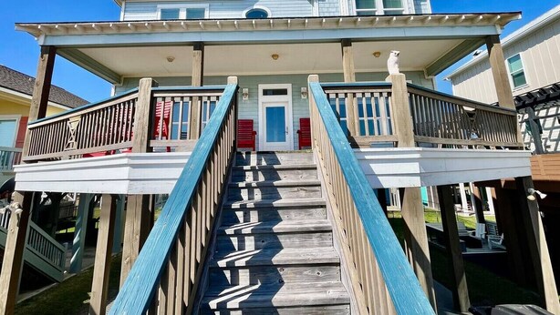 A two-story house with a front porch, a staircase, and a small balcony. - Beachfront • Sleeps 16 • King Bed • 6 Queens (Bolivar Peninsula)