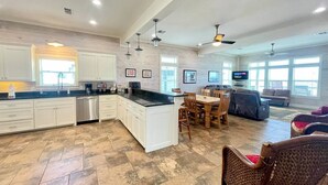 A spacious kitchen with white cabinetry, a central island, and a dining area with wooden chairs. - Beachfront • Sleeps 16 • King Bed • 6 Queens (Bolivar Peninsula)