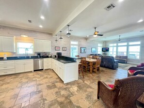 A spacious kitchen with white cabinetry, a central island, and a dining area with wooden chairs. - Beachfront • Sleeps 16 • King Bed • 6 Queens (Bolivar Peninsula)