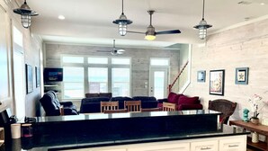 A kitchen with a black countertop, white cabinets, and a dining area with a wooden table and chairs. - Beachfront • Sleeps 16 • King Bed • 6 Queens (Bolivar Peninsula)