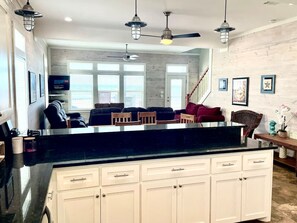 A kitchen with a black countertop, white cabinets, and a dining area with a wooden table and chairs. - Beachfront • Sleeps 16 • King Bed • 6 Queens (Bolivar Peninsula)