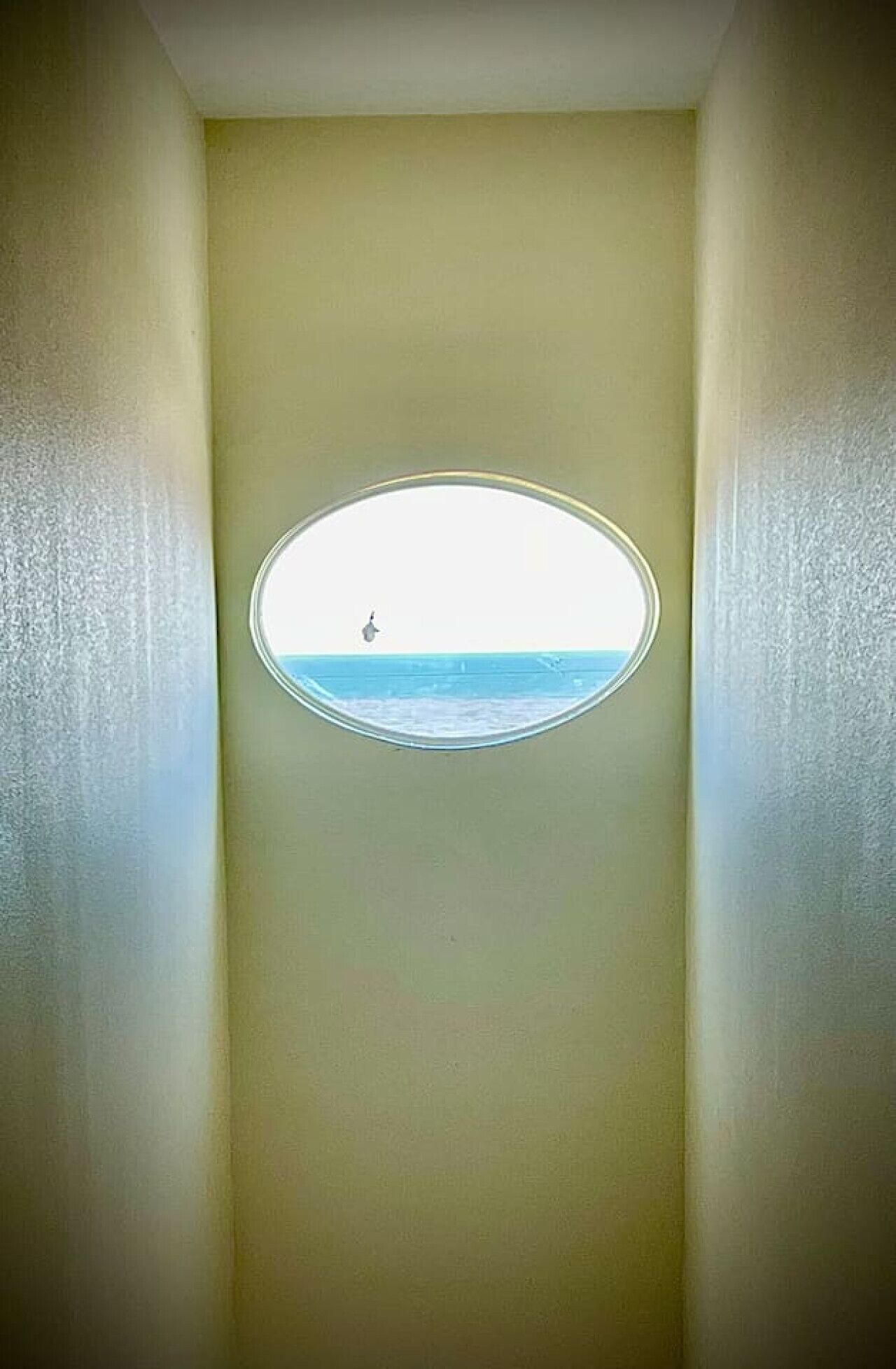 A room with a small window revealing a view of the sea.