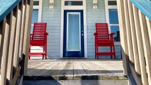 A house with a blue door, two red chairs outside, and a wooden deck. - Beachfront • Sleeps 16 • King Bed • 6 Queens (Bolivar Peninsula)