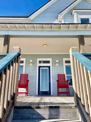A house with a blue door, two red chairs outside, and a wooden deck. - Beachfront • Sleeps 16 • King Bed • 6 Queens (Bolivar Peninsula)