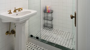 A bathroom with a pedestal sink, a glass shower enclosure, and a metal rack with toiletries. - Serene studio with AC in vibrant Los Angeles neighborhood (Los Angeles)