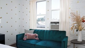 A teal sofa with a black and white polka dot pillow, a white brick wall with gold dots, and a window with white curtains. - Serene studio with AC in vibrant Los Angeles neighborhood (Los Angeles)