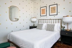 A bedroom with a bed, a nightstand, a lamp, a mirror, and two framed pictures on the wall.