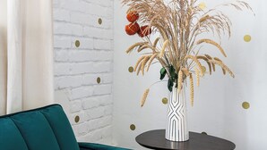 A teal sofa, a round table with a striped vase, and a white brick wall with gold dots. - Serene studio with AC in vibrant Los Angeles neighborhood (Los Angeles)