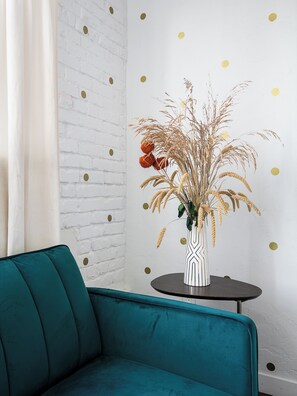 A teal sofa, a round table with a striped vase, and a white brick wall with gold dots.