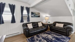 Ein Zimmer mit zwei schwarzen Ledersofas, einem blauen Teppich mit Muster, einem Gemälde an der Wand und einer Lampe.