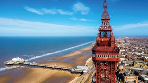 Eine Küstenstadt mit einem markanten roten Turm, einer Mole, die sich ins Meer erstreckt, und einem Strand.