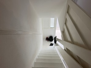 Eine weiße Treppe mit Handlauf, die zu einer Zwischenplattform führt, wo Schuhe und ein Rucksack liegen.