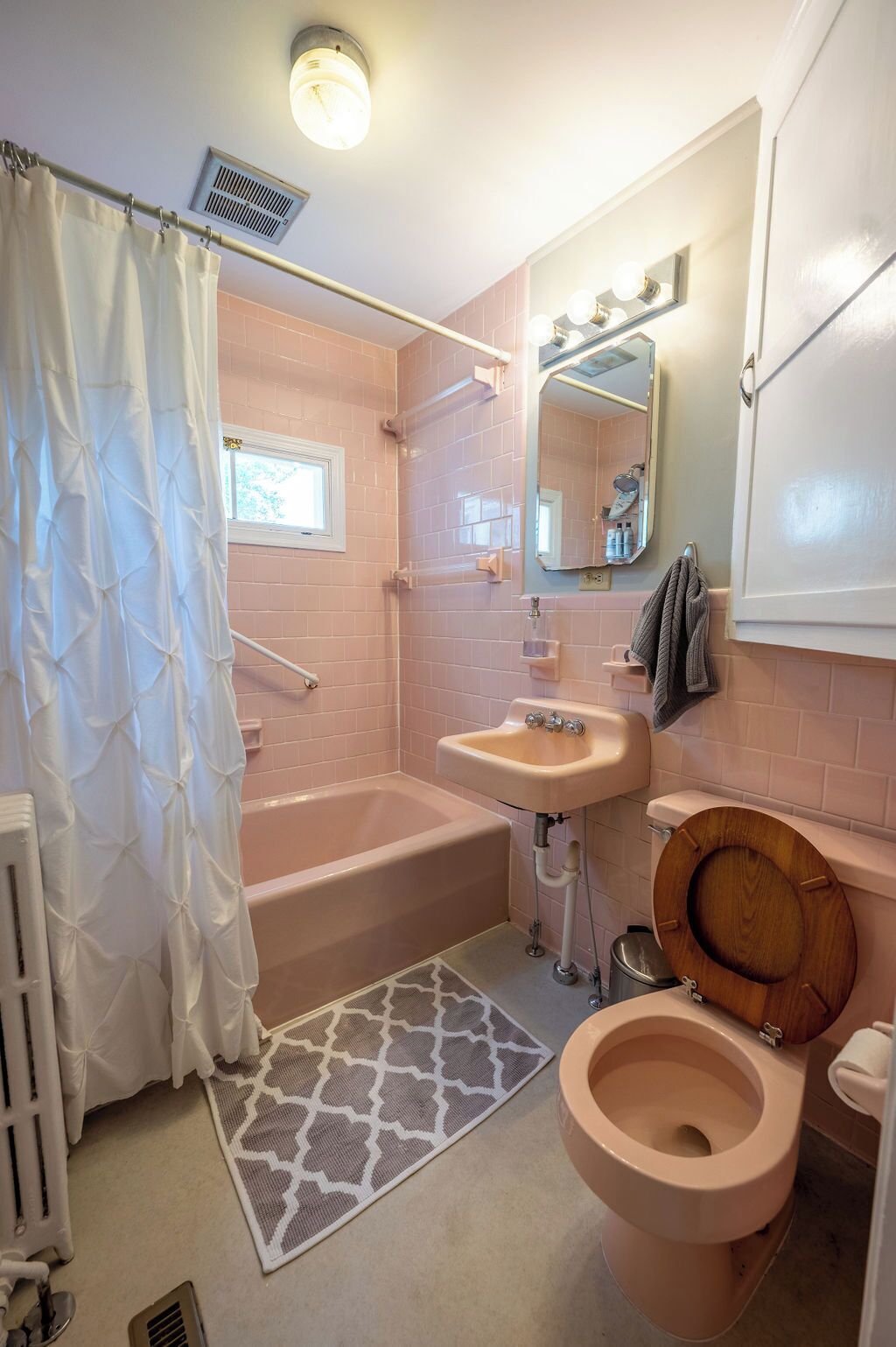 A bathroom with a bathtub, a sink, a toilet, a shower curtain, a window, and a mirror with lights.