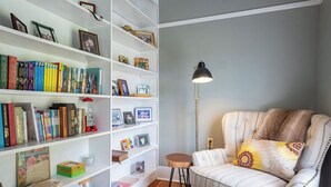 A cozy living room with a striped sofa, a small wooden stool, a patterned rug, and a bookshelf filled with books and framed photos.