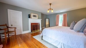 A bedroom with a bed, a wooden chair, a fireplace, and a window with curtains.