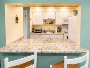 A compact kitchen with white cabinets, a granite countertop, a toaster, a sink, and a stove. - 2BR Beach Bungalow | Walk to Beach | Sleeps 5 (Norfolk)